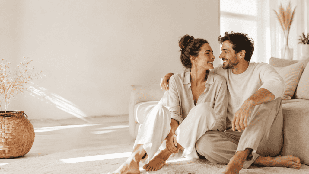 Couple heureux et complice assis dans un salon lumineux, illustrant le bien-être dans le couple, la confiance, l’énergie et la vitalité au quotidien.