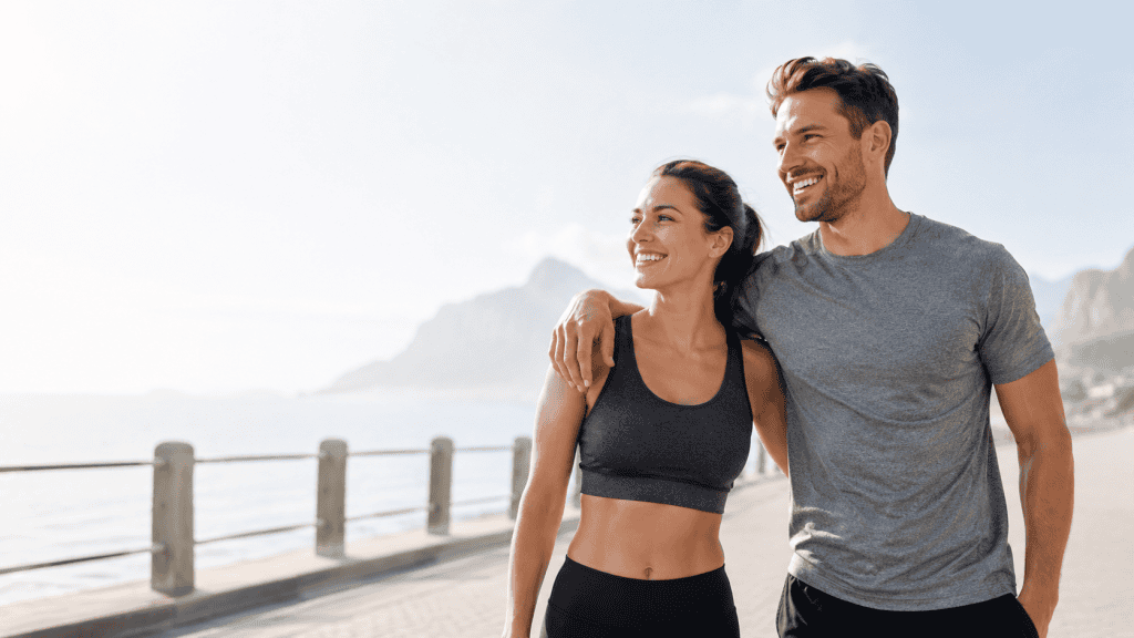 Couple sportif souriant au bord de l’eau, illustrant l’énergie, la vitalité, la confiance et le bien-être dans une routine active.